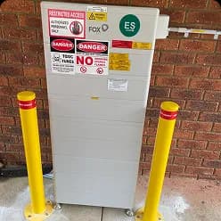 Fox ESS battery with yellow bollards against a red brick wall in Leda, WA