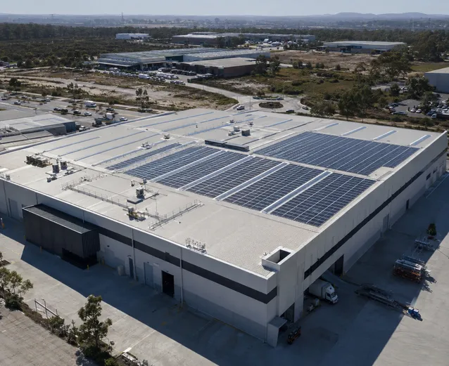 Aerial view of large commercial warehouse with extensive solar panel array installation on flat roof in industrial district. 
