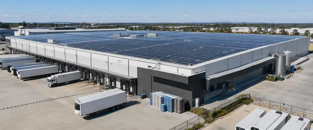 Large distribution center with extensive rooftop solar panel array and multiple loading docks with semi-trailers.